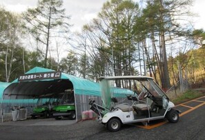 A golf cart parked in front of a tent with a sign, trees in the background, and a paved area.