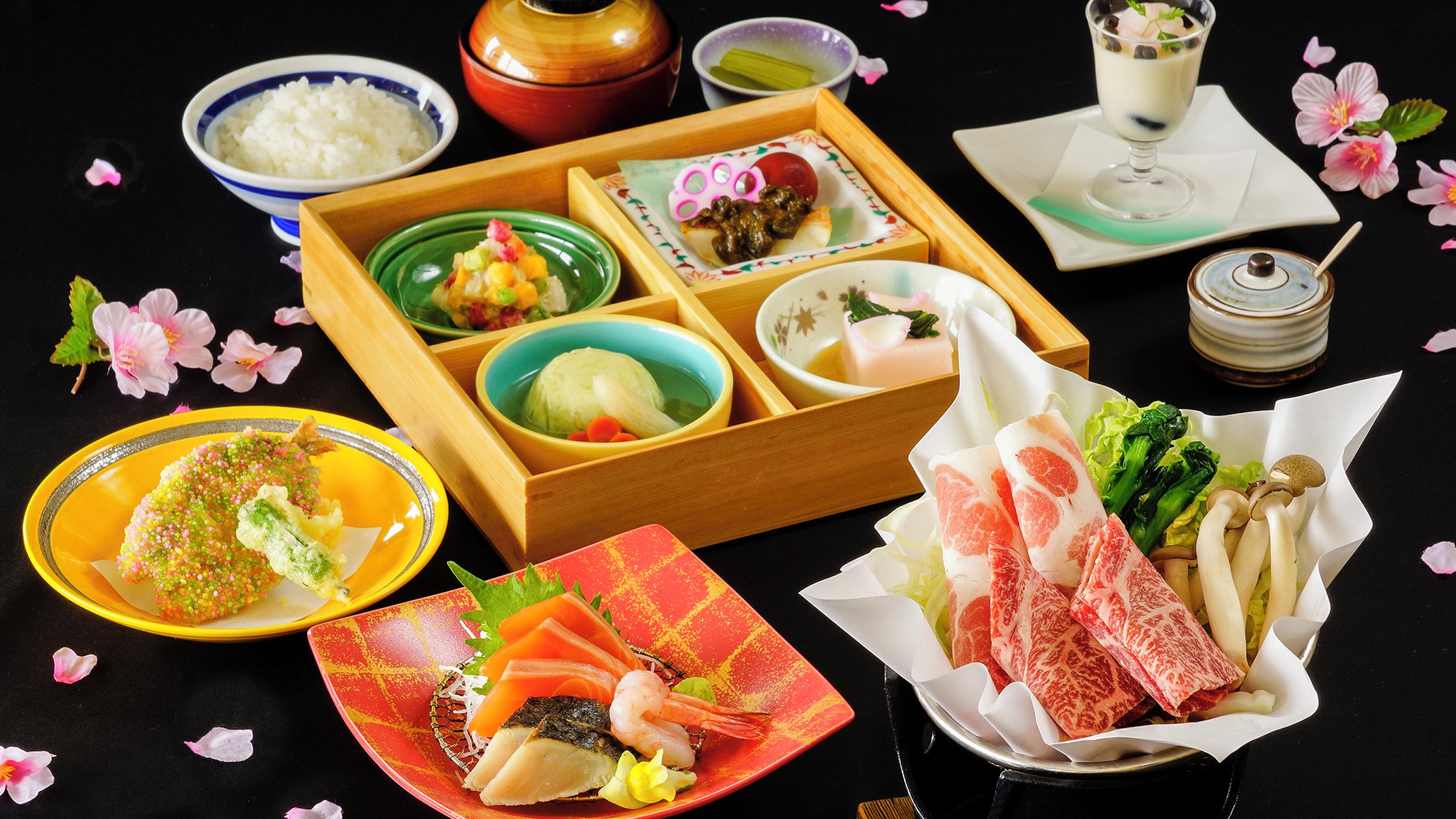 A variety of Japanese dishes arranged on a table with a black background.
