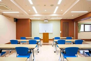A classroom with desks and chairs arranged in rows, a projector screen at the front, and a door on the right. - Ageo Tobu Hotel (Ageo)