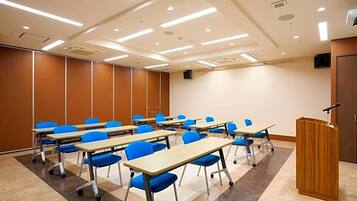 A conference room with multiple tables and chairs, a podium, and a speaker on the wall.