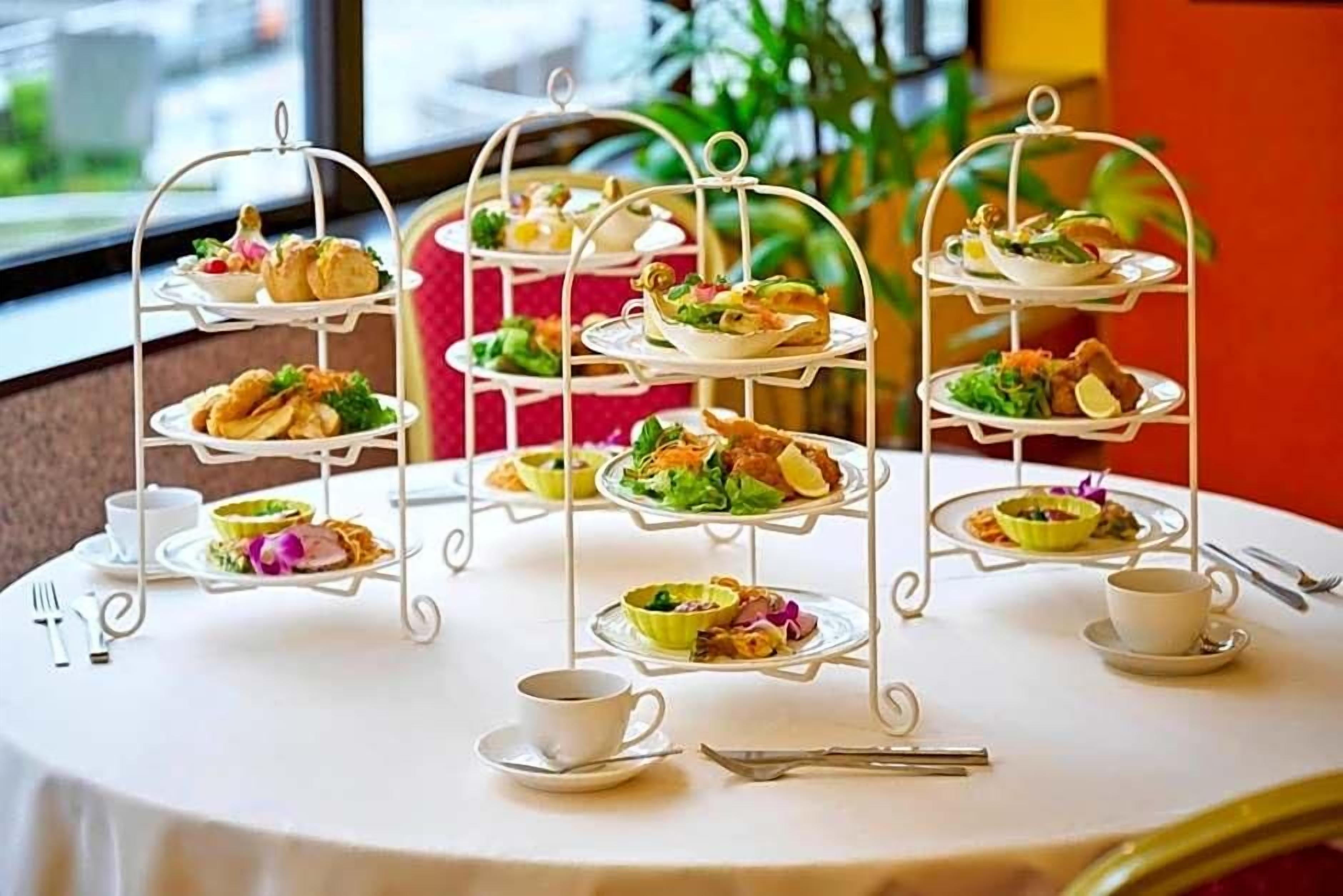 A three-tiered outdoor tea service with various dishes and a cup of tea on a round table.