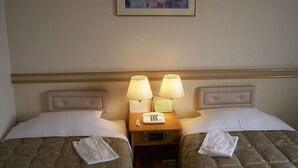 A hotel room with two beds, each with a pillow and a folded towel. There is a nightstand with two lamps and a phone between the beds. A framed picture hangs on the wall above the beds. - Ageo Tobu Hotel (Ageo)