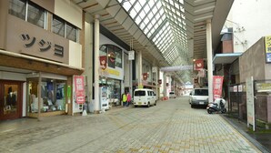 A covered pedestrian walkway with shops on either side, a van, and a scooter parked on the right.
