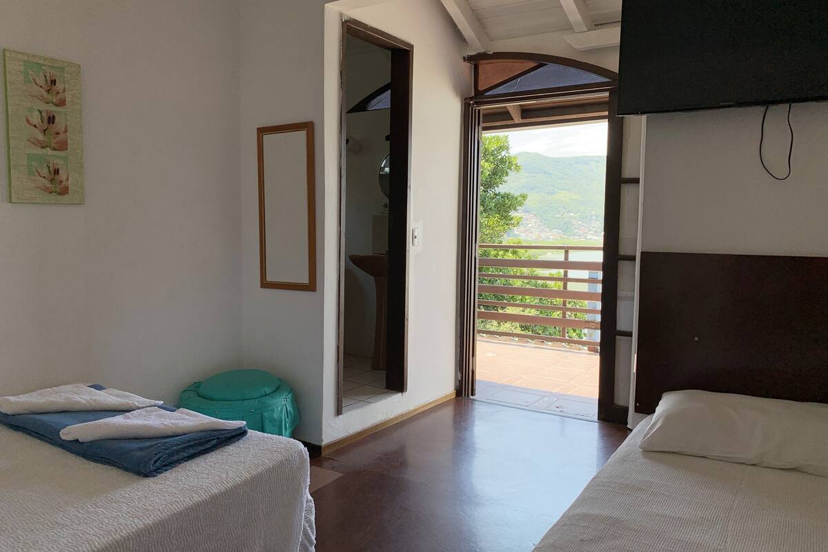 Ein Hotelzimmer mit zwei Betten, einem durchgegangenen Tür erkennbaren Badezimmer und einem Balkon mit Blick auf die Landschaft.