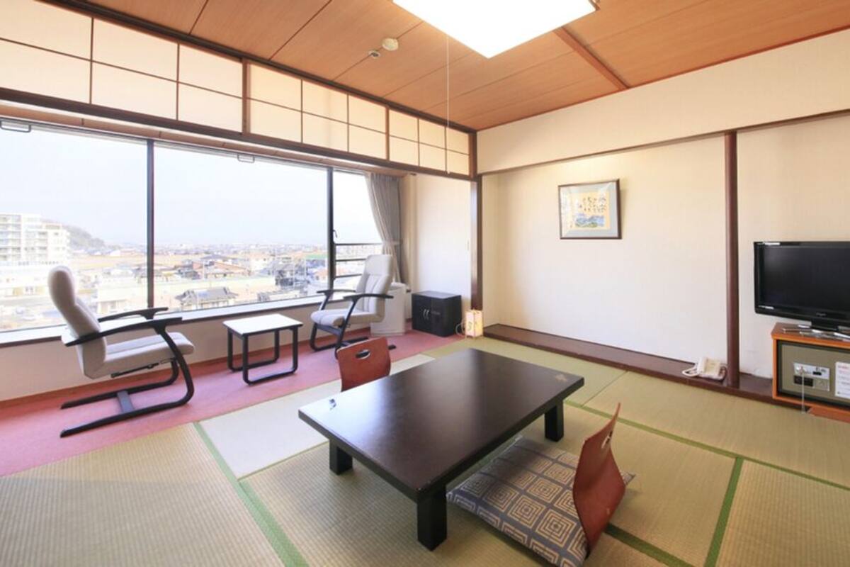A room with tatami flooring, a sofa, a table, a TV, and a city view.