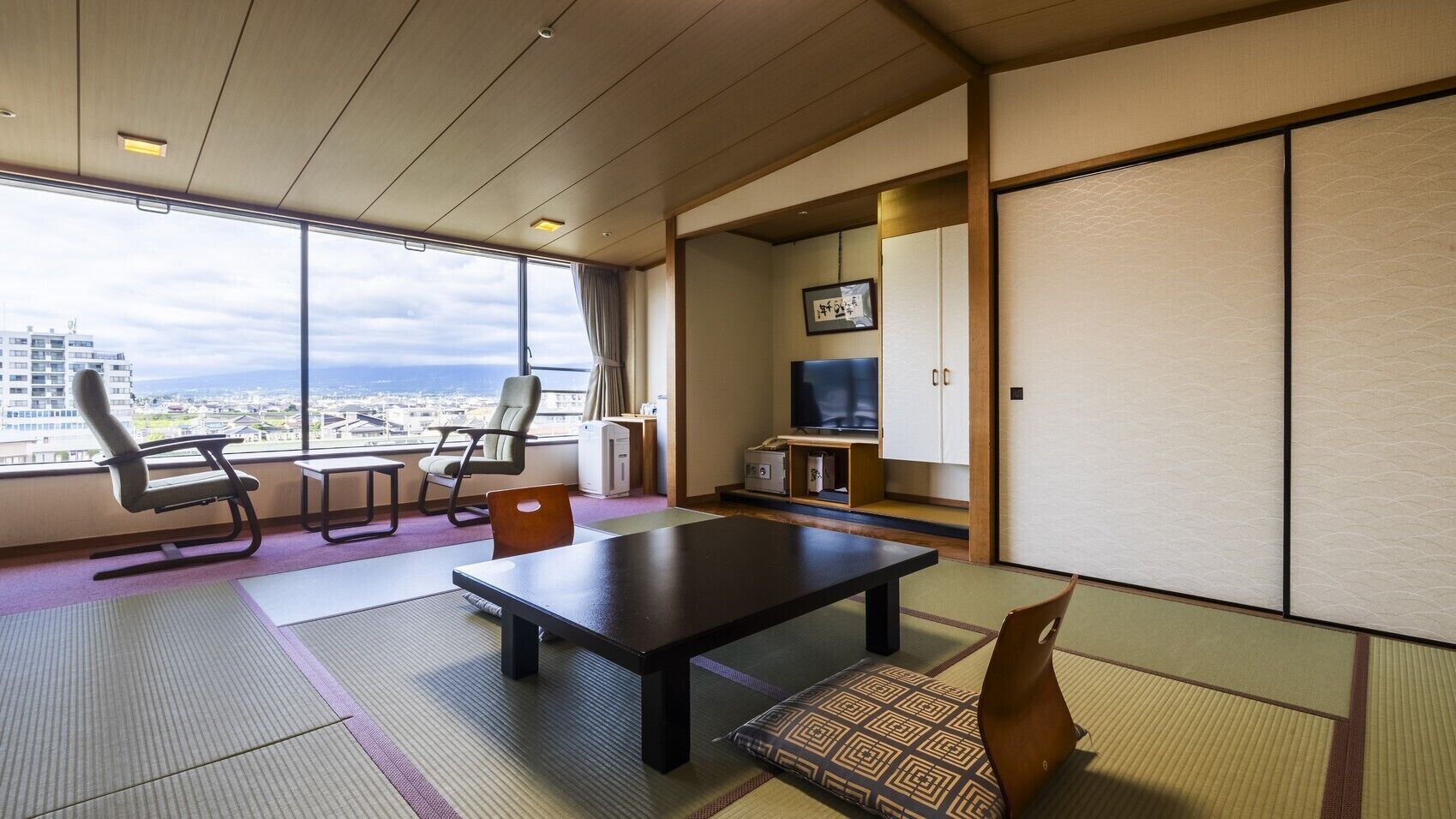 A room with tatami mats, a low table, chairs, a television, and a sliding door.