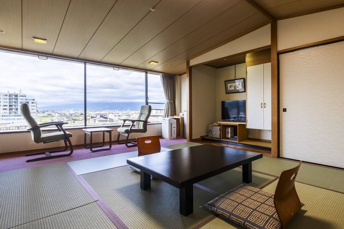 A room with tatami mats, a low table, chairs, a television, and a sliding door.