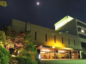 Un hotel amb façana moderna, entrada il·luminada i indicadors en una llengua estrangera.