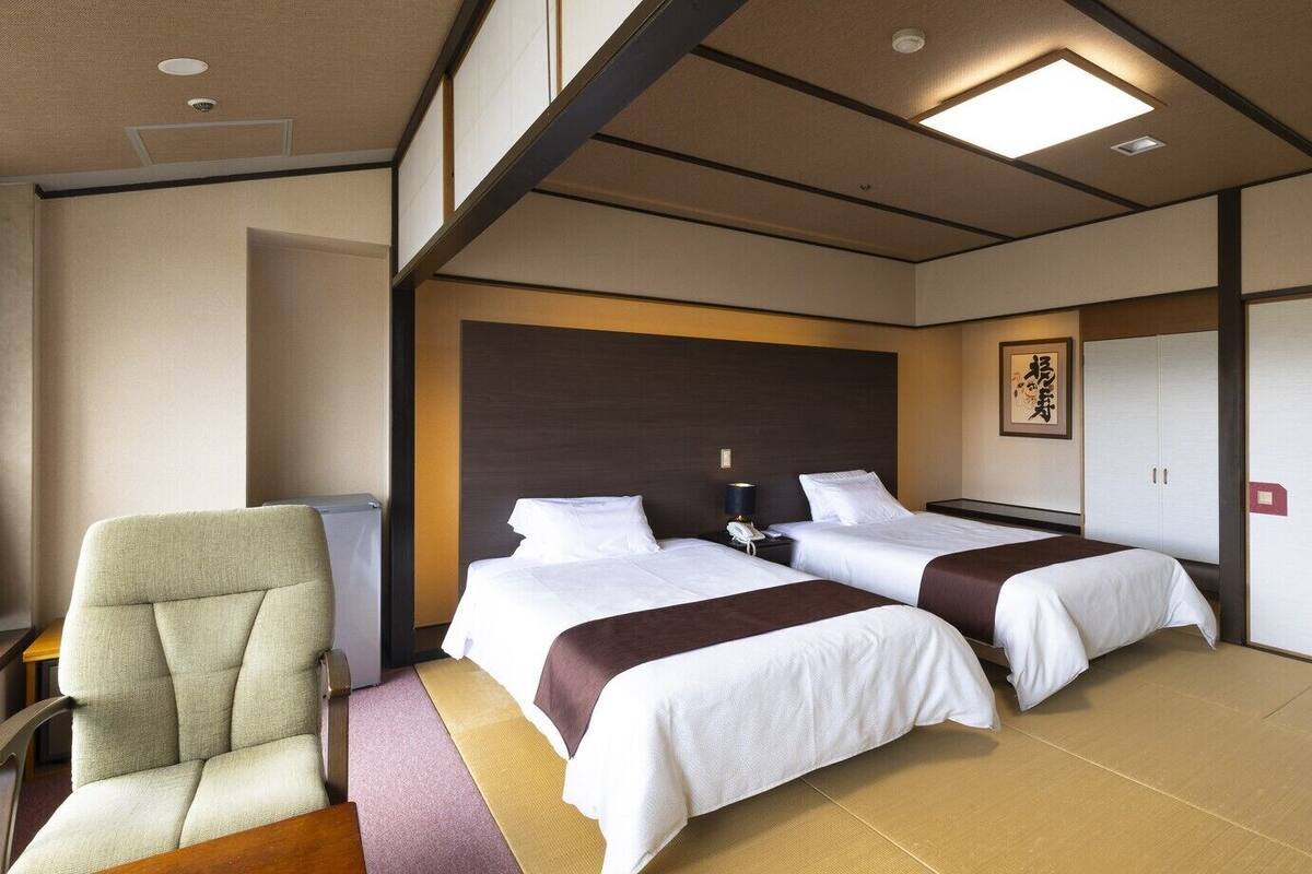 A hotel room with two beds, a chair, a desk, and a wall-mounted phone.