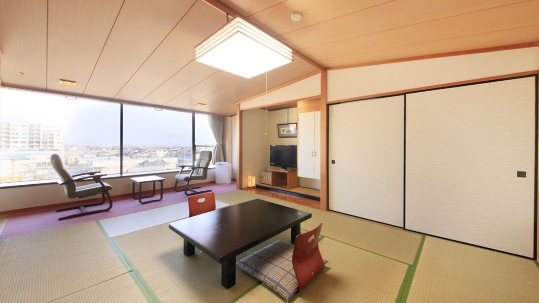 A hotel room with tatami mats, a low table, chairs, a television, and sliding doors.