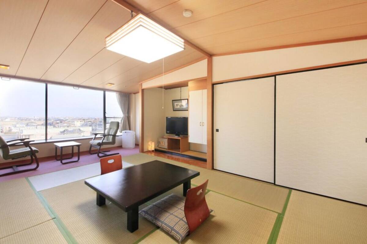 A hotel room with tatami mats, a low table, chairs, a television, and sliding doors.