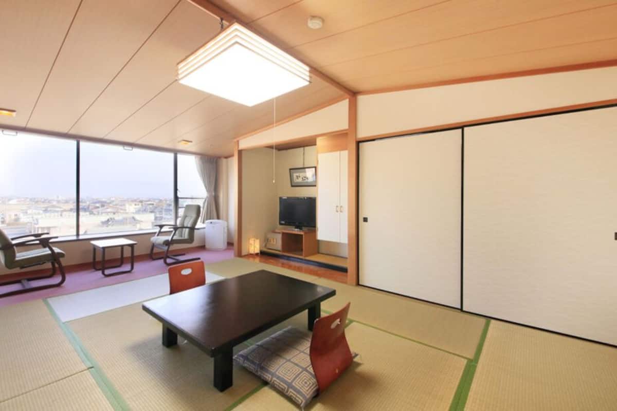 Habitación de hotel con esteras de tatami, una mesa baja, sillas, un televisor y puertas correderas.