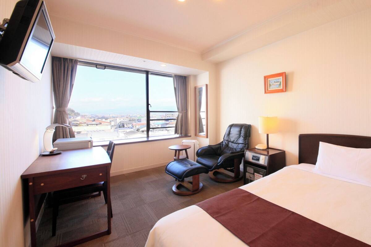 A hotel room with a bed, desk, chair, and a TV.
