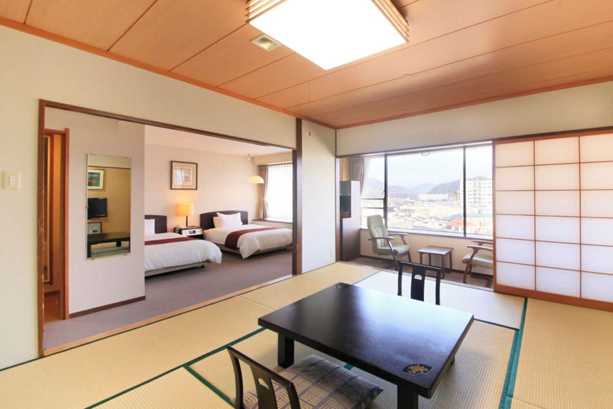 A traditional Japanese-style room with tatami flooring, a low table, a sofa, and a view of a cityscape through large windows.