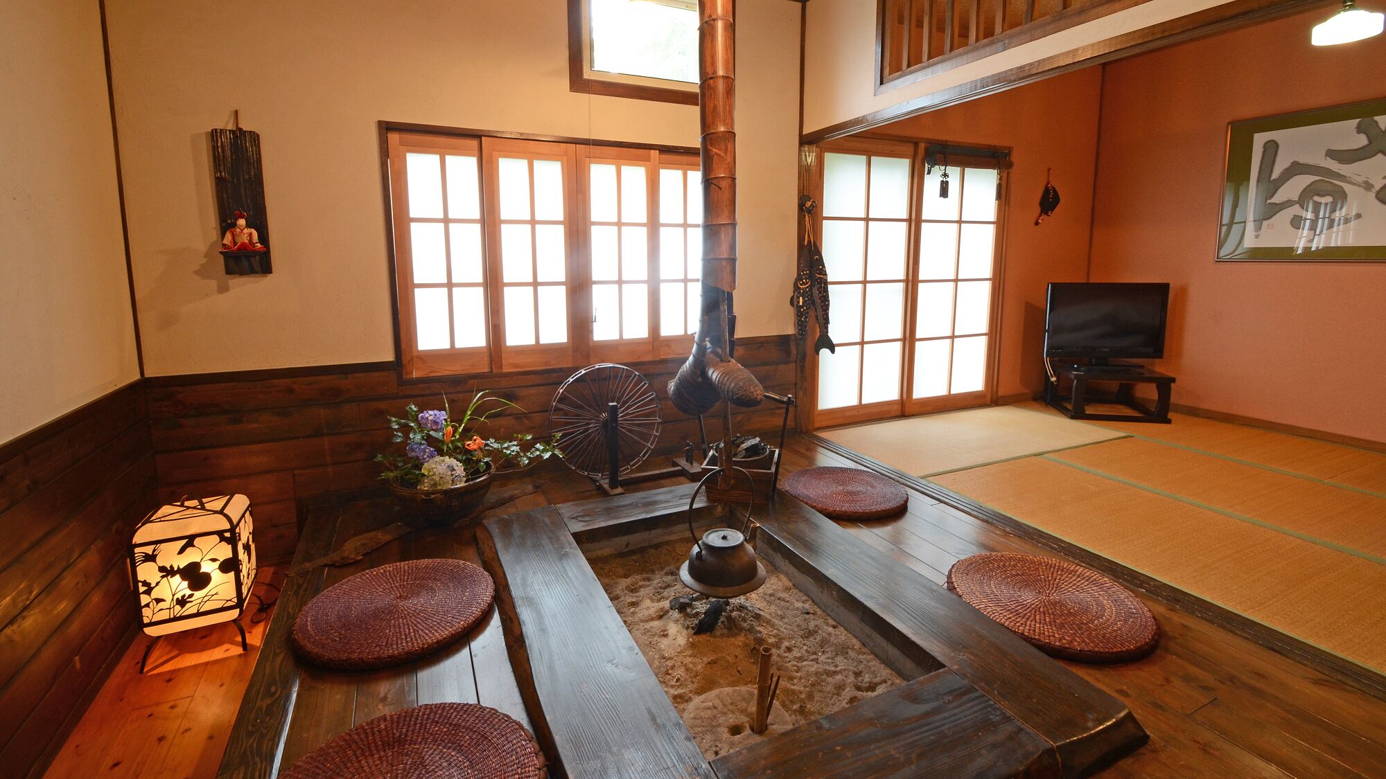 A traditional Japanese room with tatami flooring, a shoji screen, a tatami mat table, a hanging tatami mat, a traditional Japanese lantern, and a television.