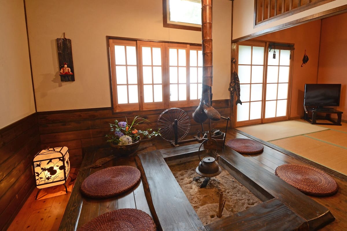 A traditional Japanese room with tatami flooring, a shoji screen, a tatami mat table, a hanging tatami mat, a traditional Japanese lantern, and a television.