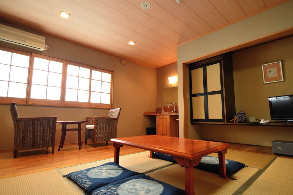 A traditional Japanese-style room with tatami mats, a low table, a television, and a cabinet.