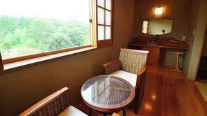 A room with a round glass table, wicker chairs, a wooden desk, and a window with a view of trees. - Shikisai no Sato Manyuu (Kirishima)