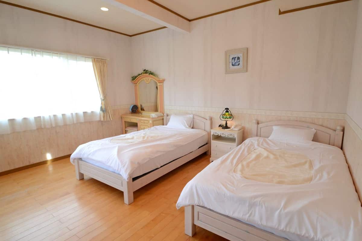 A hotel room with two beds, a vanity with a mirror, a bedside table with a lamp, and a framed picture on the wall.