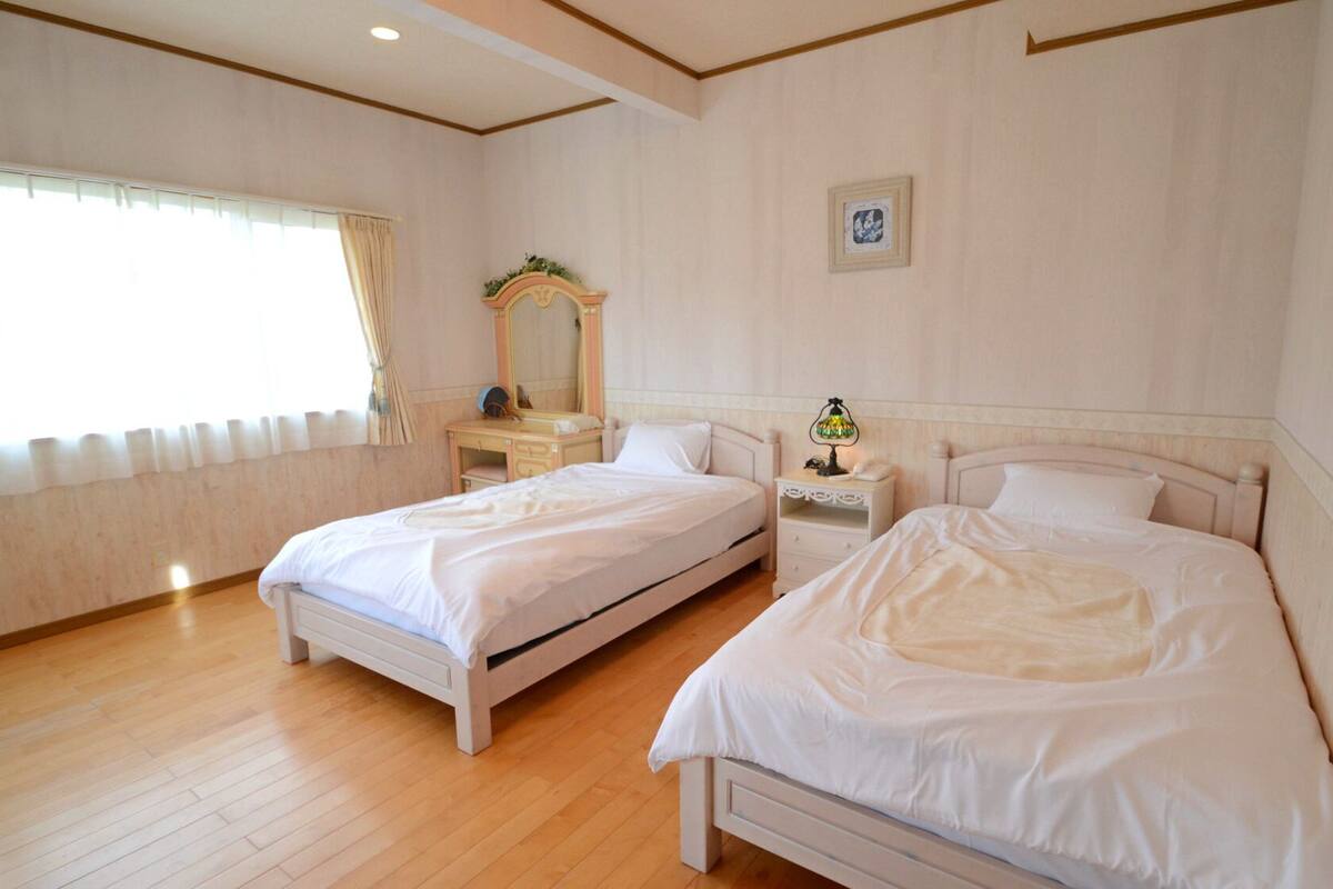 A hotel room with two beds, a vanity with a mirror, a bedside table with a lamp, and a framed picture on the wall.