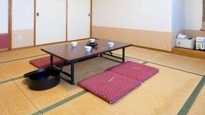 A tatami mat room with a low table, cushions, and a traditional Japanese room divider. - Shikokuya (Saijo)