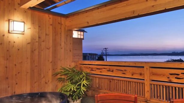 Una terraza de madera con un jacuzzi, sillas y vista al agua.