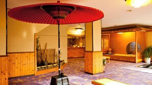 Un interior japonés tradicional con suelo de tatami, una sombrilla roja y una zona de recepción.