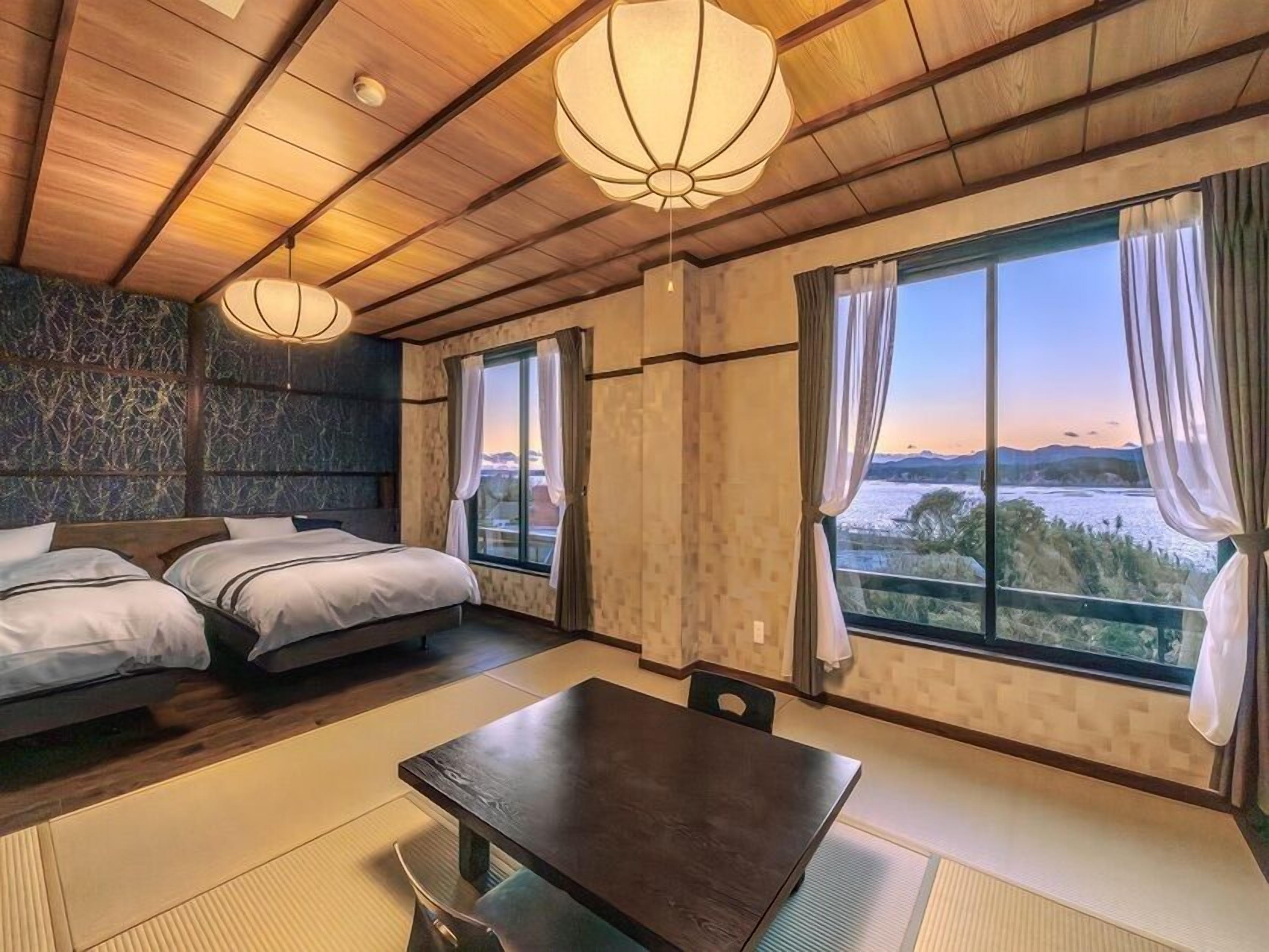 Habitación de hotel con cama, mesa de comedor y ventanas amplias que ofrecen vistas.