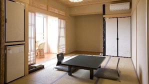 Una habitación japonesa tradicional con suelo de tatami, una mesa baja, una silla, una puerta corrediza y un ventilador de techo.