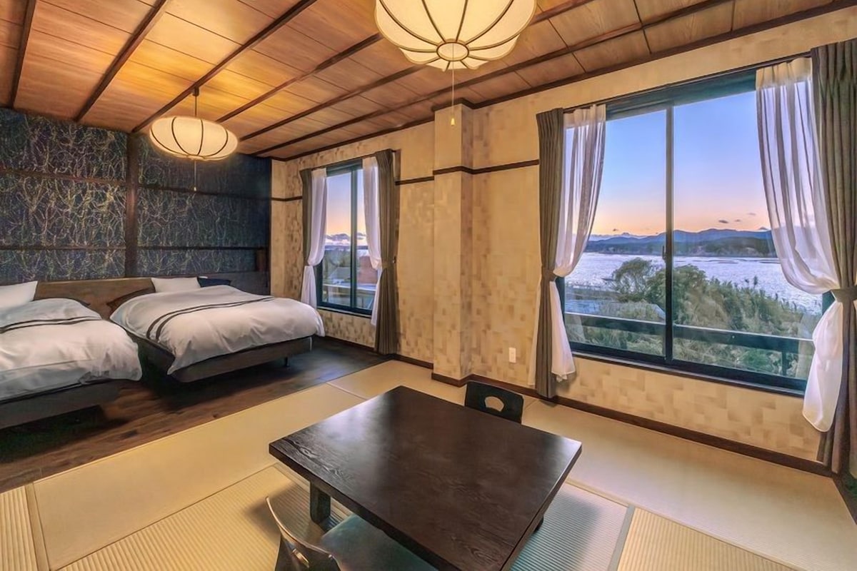 Habitación de hotel con cama, mesa de comedor y ventanas amplias que ofrecen vistas.