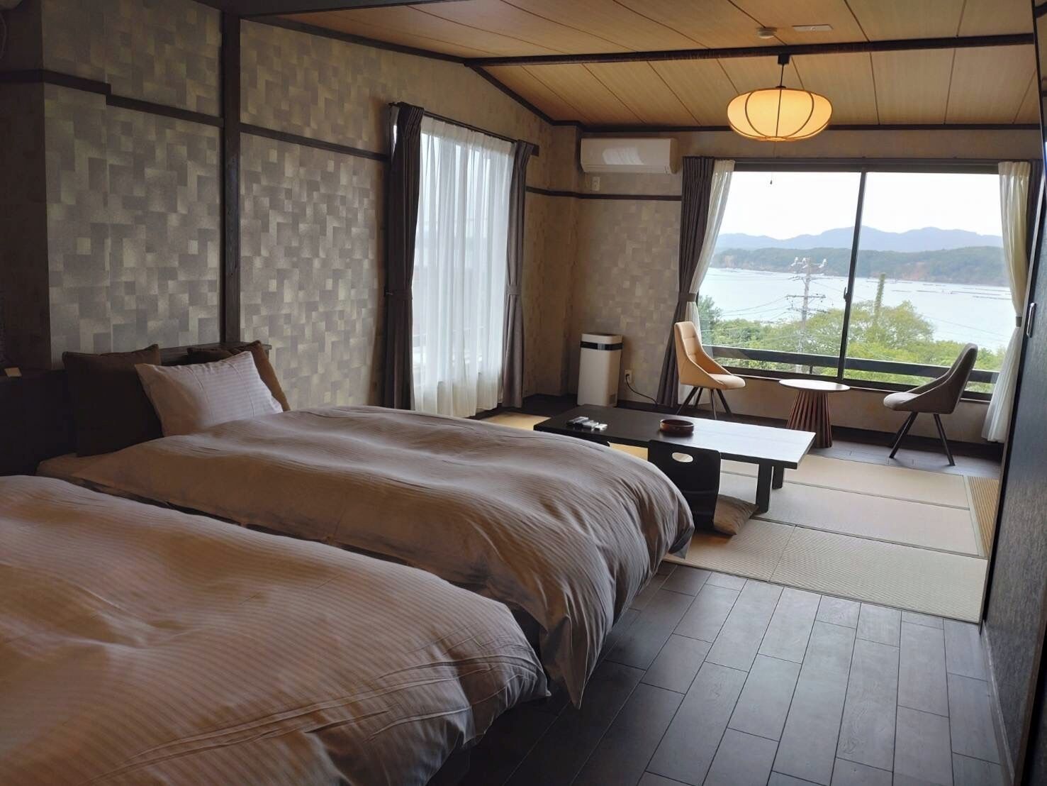 Un dormitorio con una cama grande, un escritorio y una silla, con vistas a un cuerpo de agua y montañas.