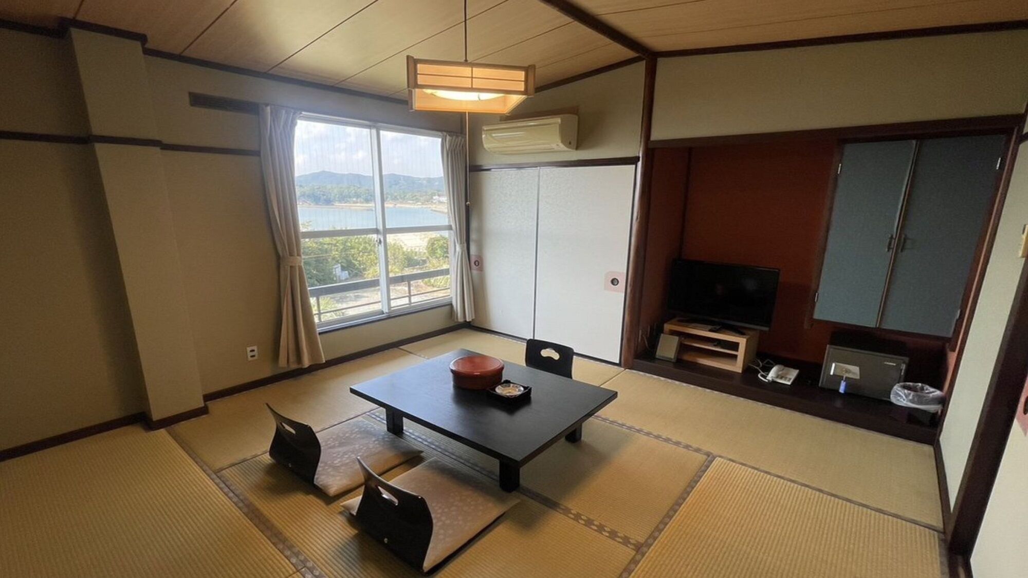 Una habitación con suelo de tatami, una mesa baja con cojines, una televisión y vistas al exterior.