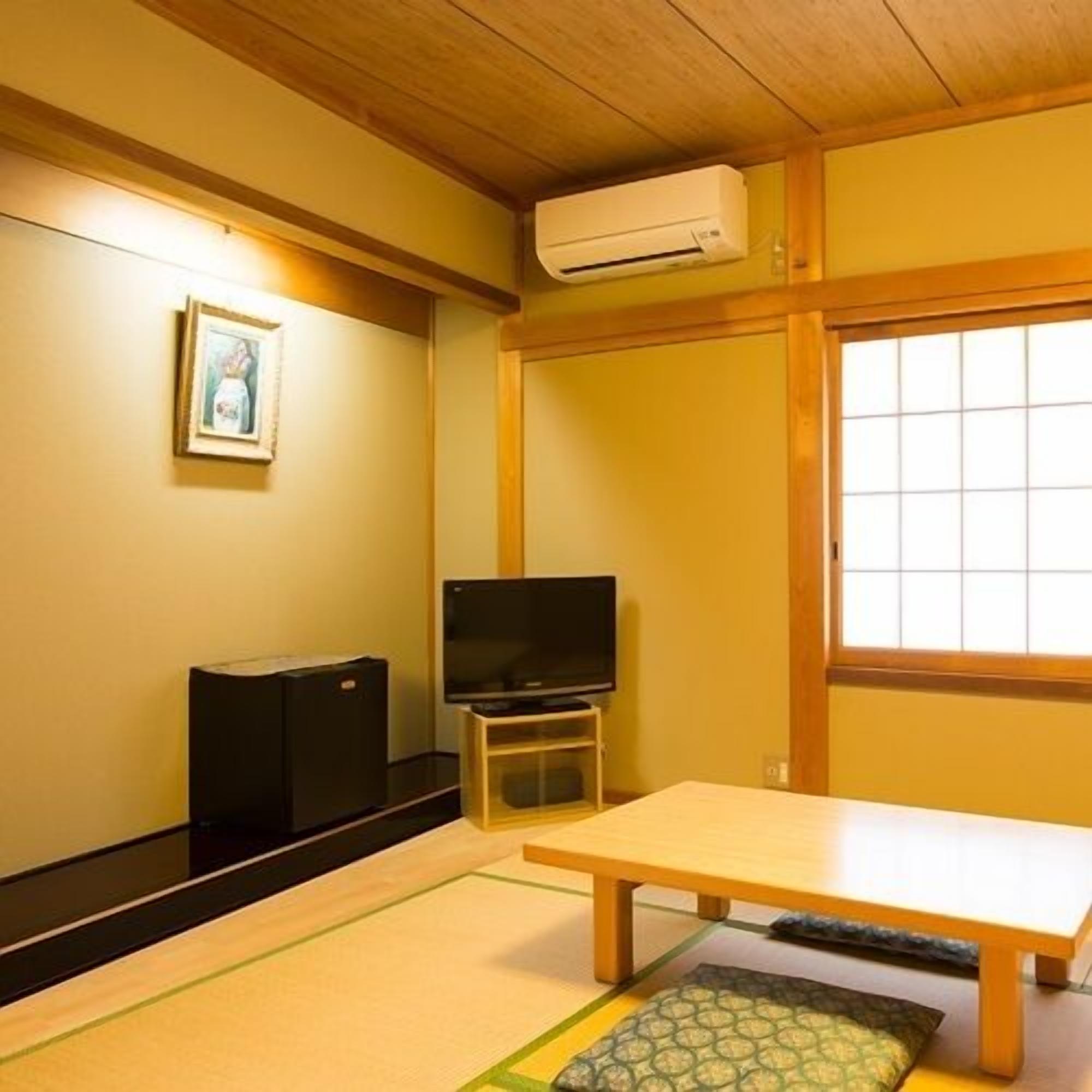 Una habitación japonesa tradicional con suelo de tatami, una mesa baja, un televisor sobre un soporte y un puertas correderas.