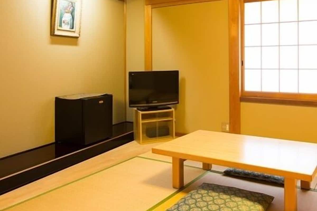 A traditional Japanese room with tatami flooring, a low table, a television on a stand, and a sliding door.