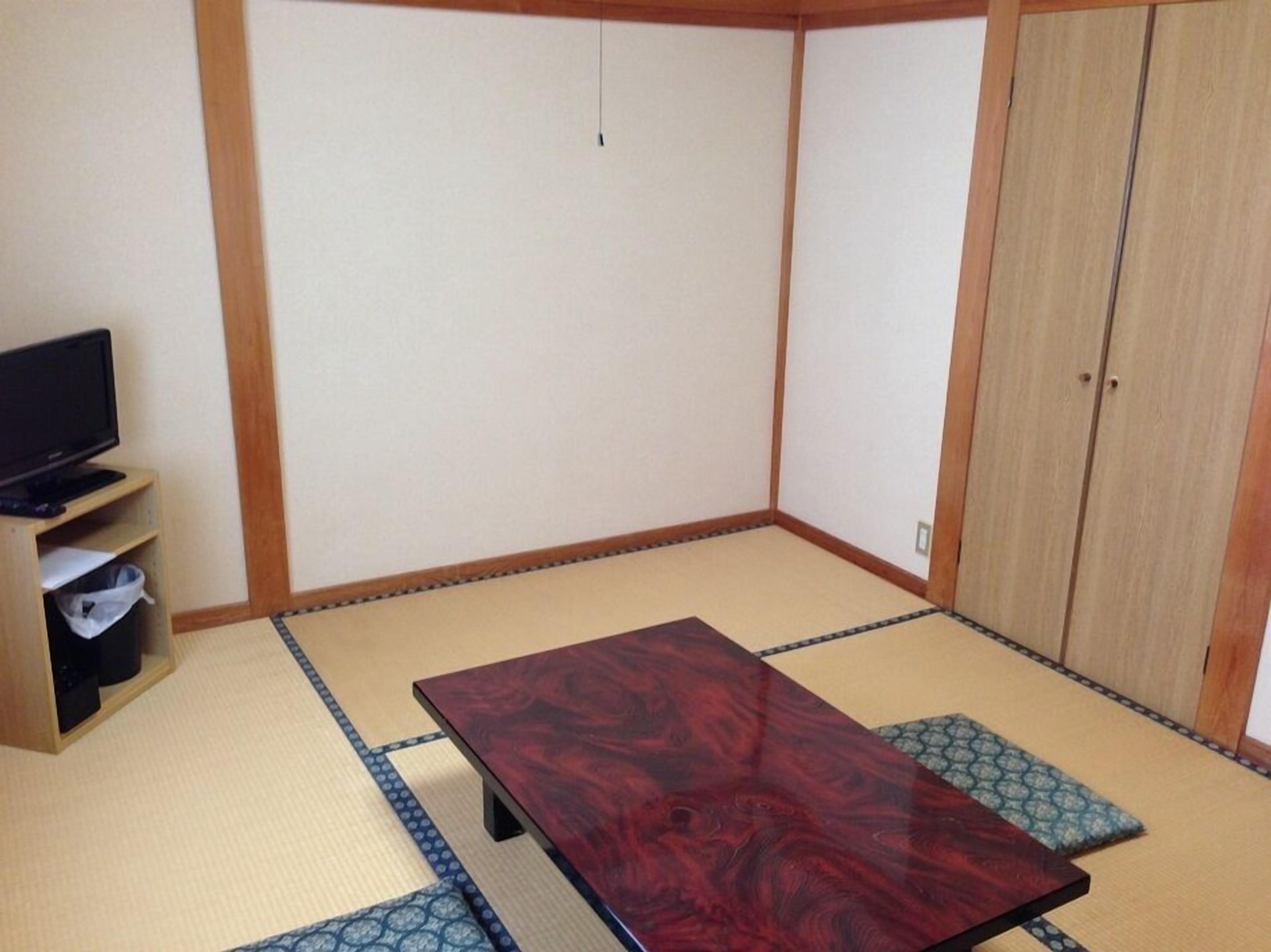 Una habitación con suelo de tatami, una mesa de madera, un televisor en un estante y un armario.