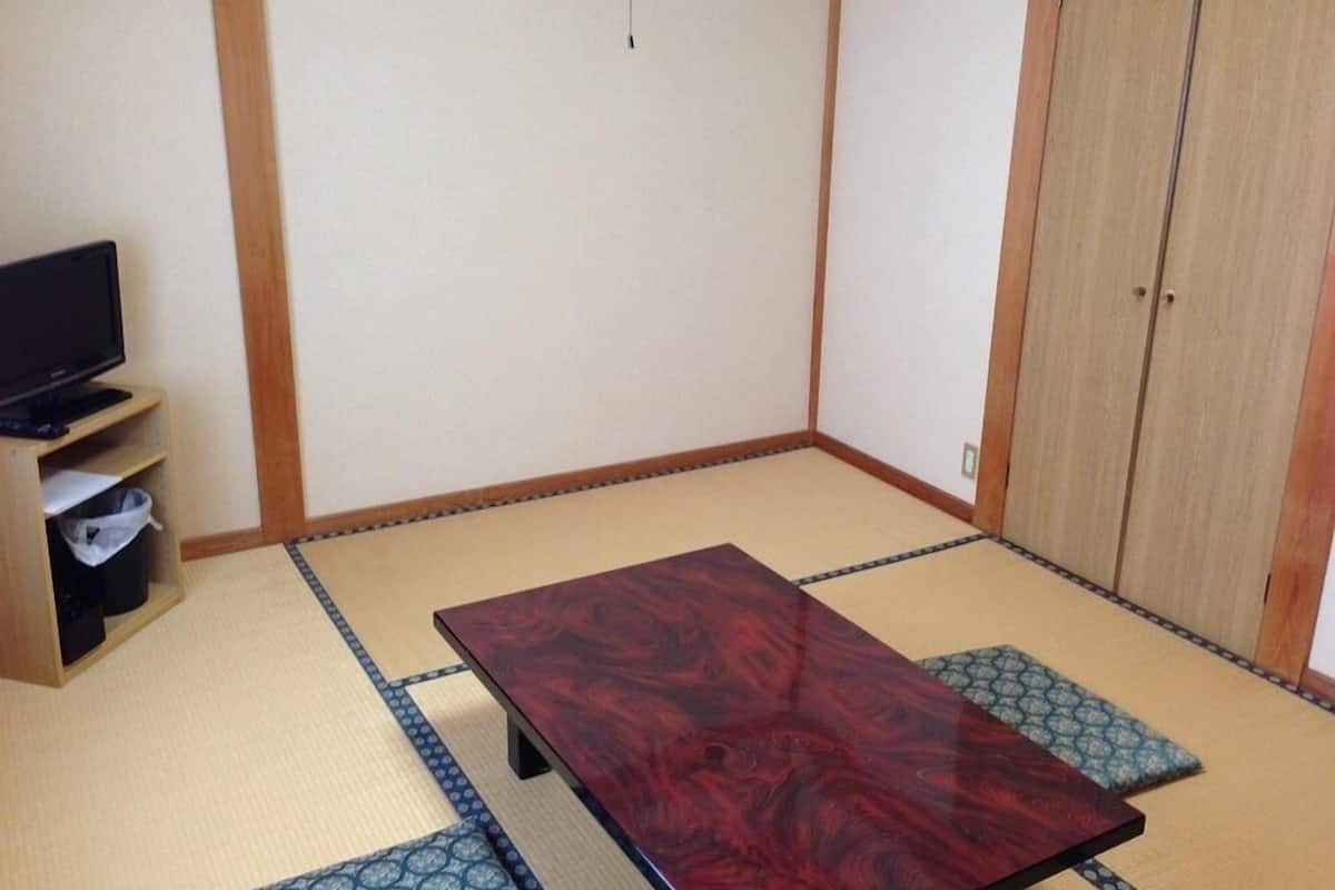 A room with tatami flooring, a wooden table, a television on a shelf, and a wardrobe.