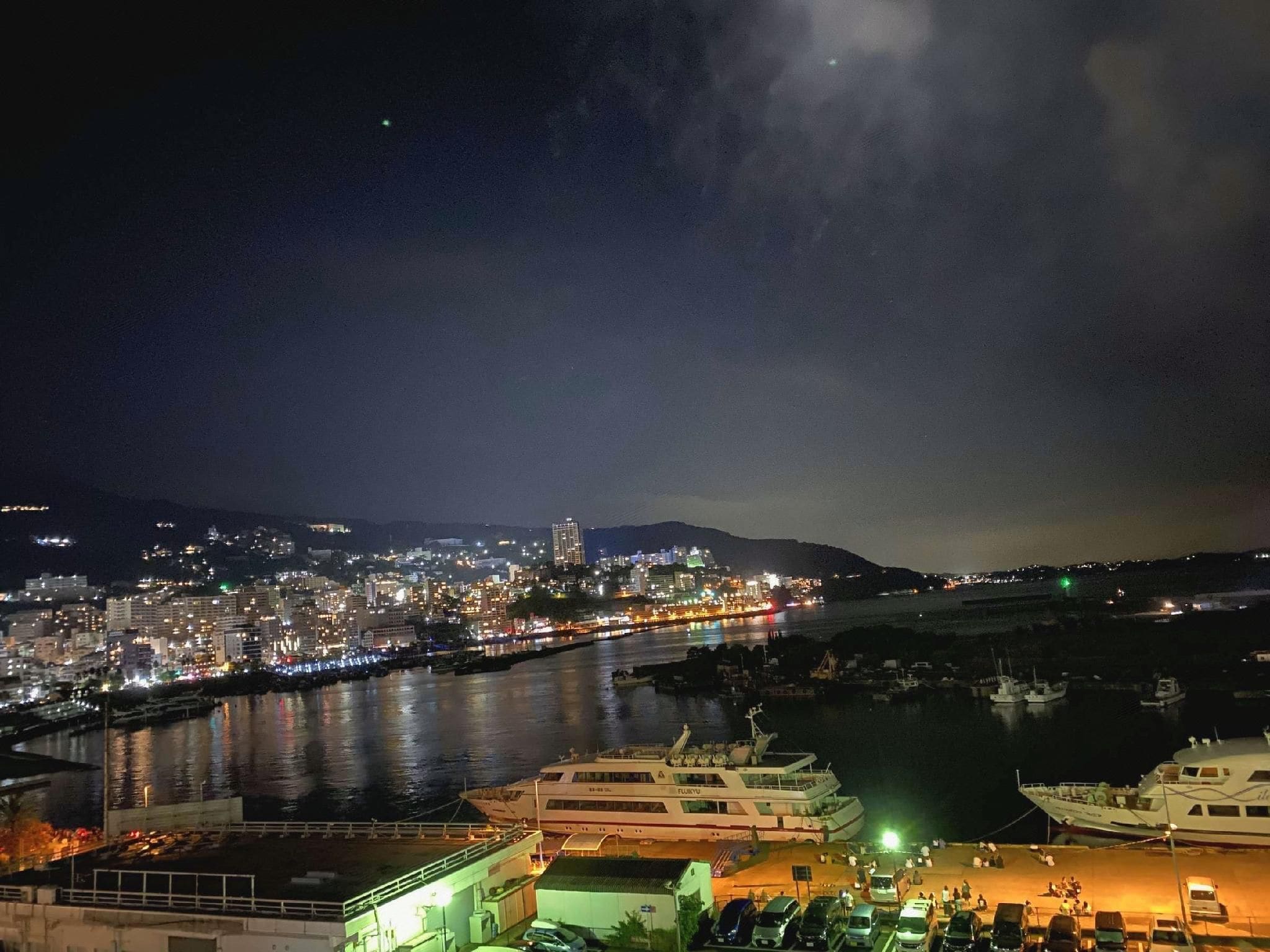 Une vue nocturne d’une ville, avec une rivière, des bateaux et une zone portuaire.