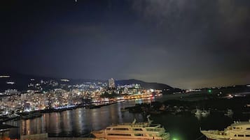 Une vue nocturne d’une ville, avec une rivière, des bateaux et une zone portuaire.