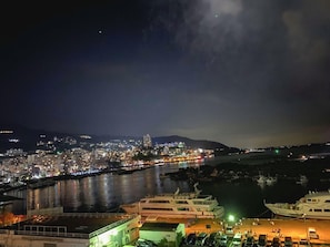 A nighttime cityscape with a river, boats, and a dock area.