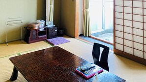A traditional Japanese room with tatami flooring, a low table, a chair, a sliding door, and a ceiling fan. - Atami Minoya Hotel (Atami)