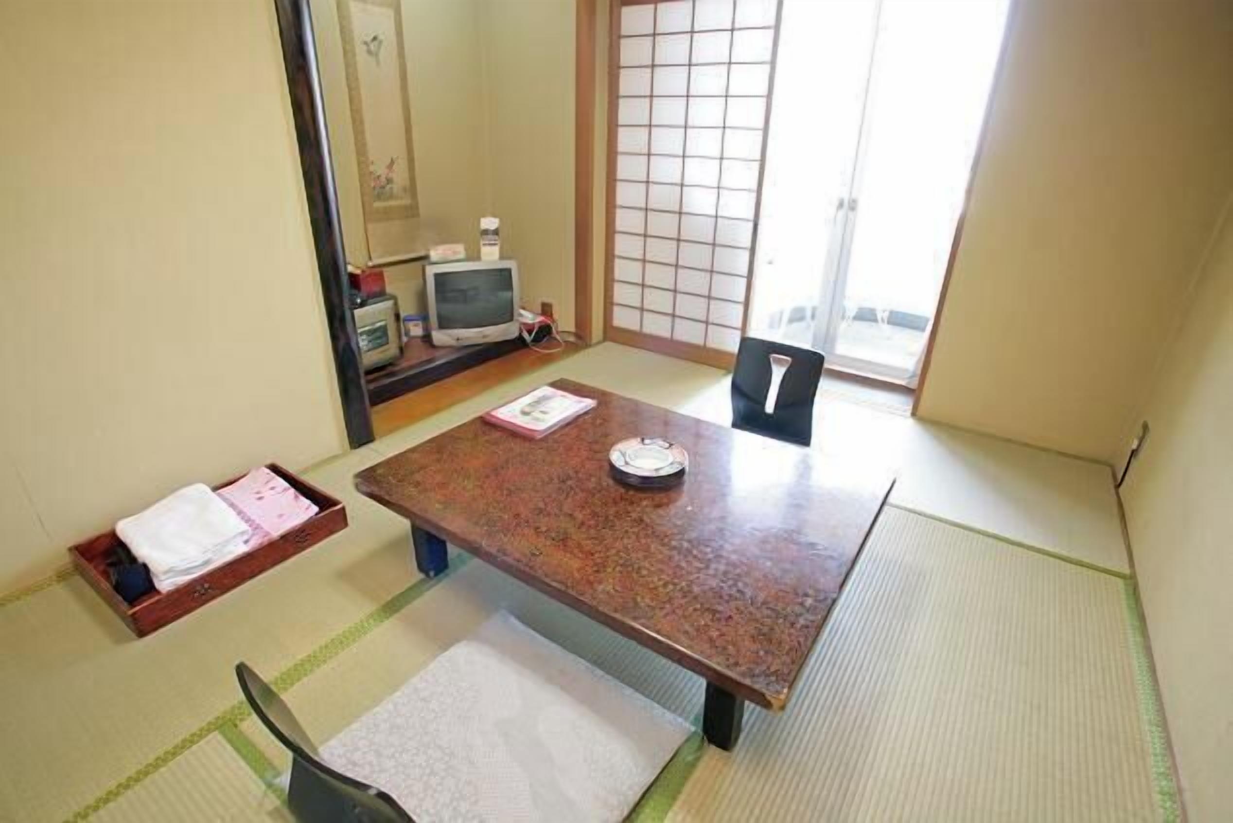 A traditional Japanese room with tatami flooring, a low table, a chair, and a sliding door.