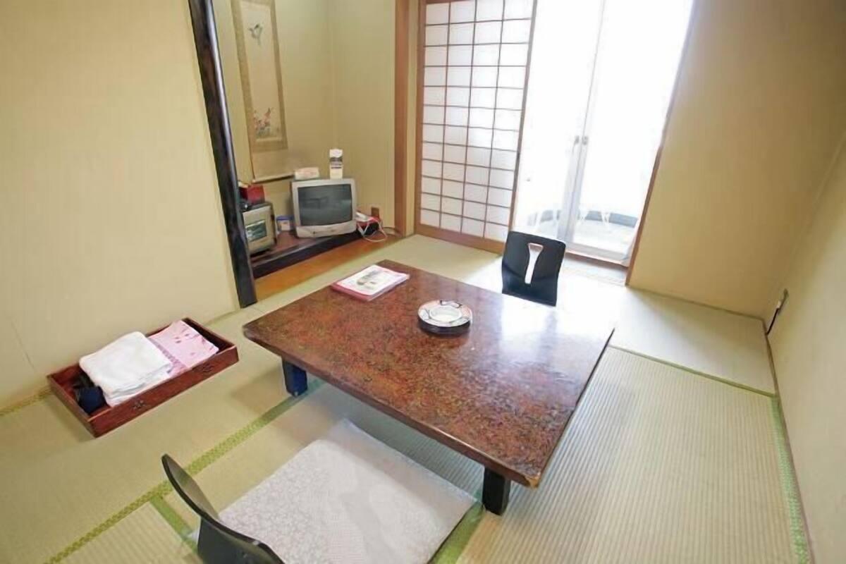 A traditional Japanese room with tatami flooring, a low table, a chair, and a sliding door.