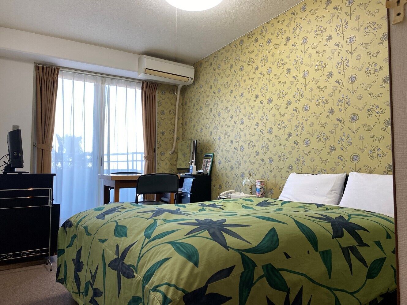 A hotel room with a bed, desk, chair, and an air conditioning unit.