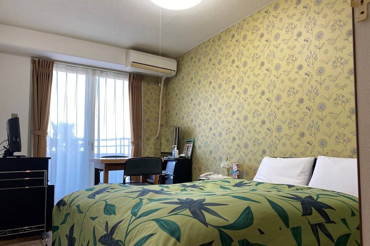 A hotel room with a bed, desk, chair, and an air conditioning unit.