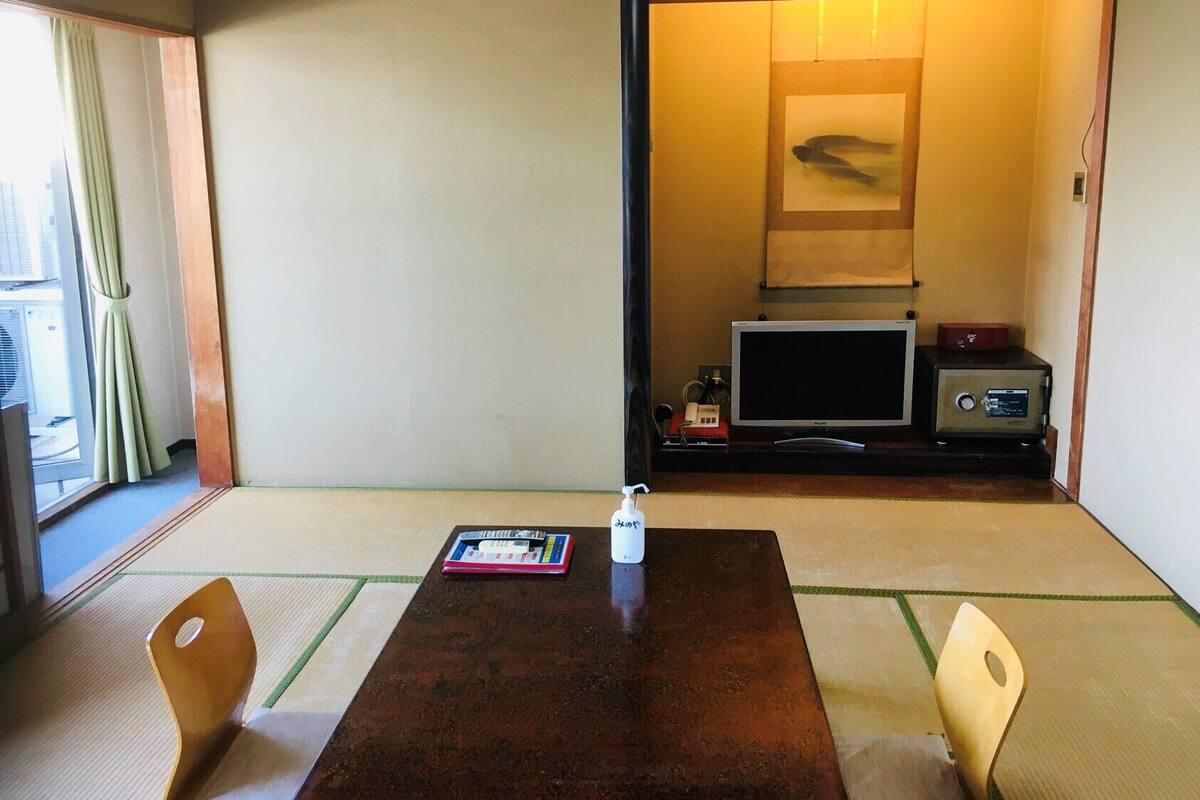 A traditional Japanese room with tatami flooring, a wooden table, two chairs, a television, and a safe.