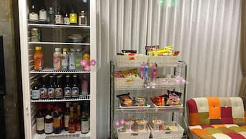 Un réfrigérateur rempli de boissons et d’en-cas, un distributeur automatique proposant divers articles, et une chaise colorée.