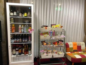 A refrigerator stocked with beverages and snacks, a vending machine with various items, and a colorful chair.