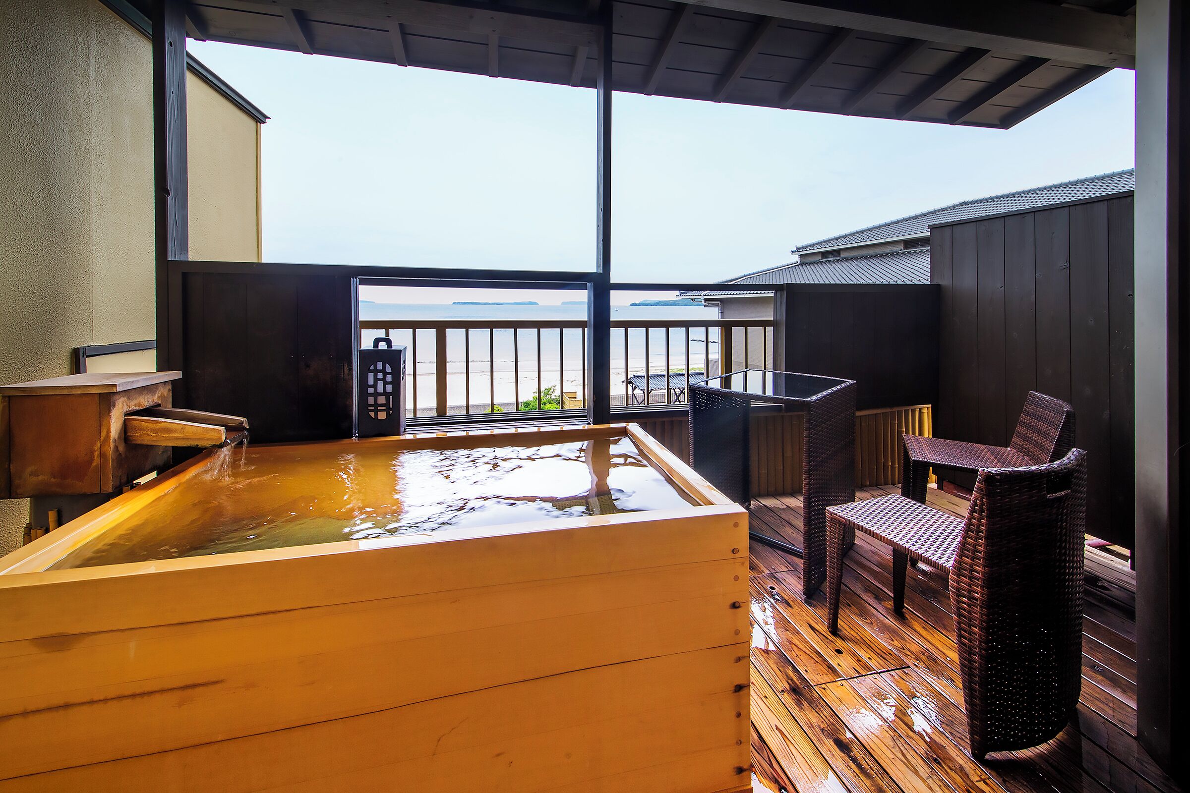 Una bañera de madera con vistas al mar, una silla de mimbre y una cubierta de madera.