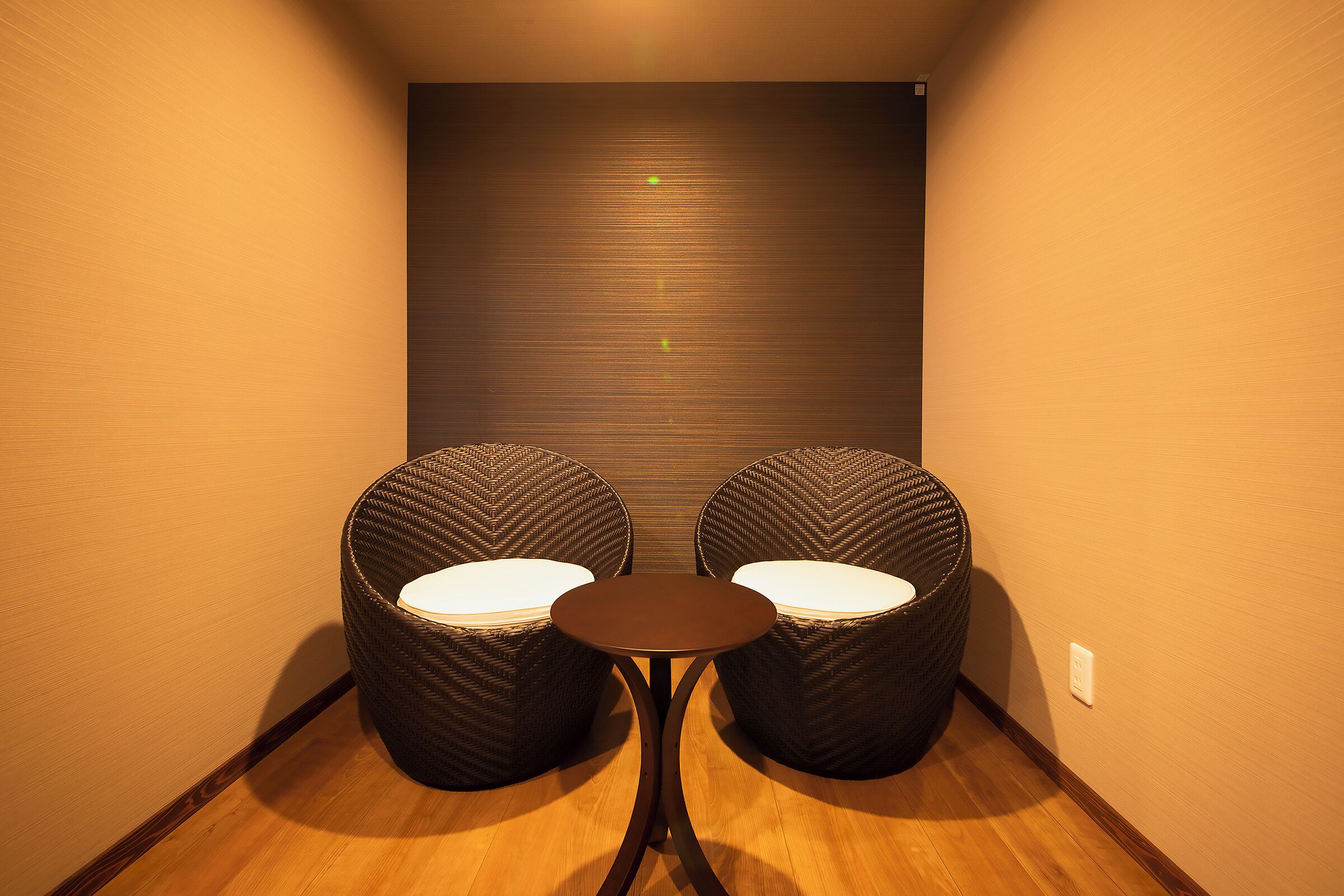 Una habitación pequeña con dos sillas de mimbre y una mesa redonda.