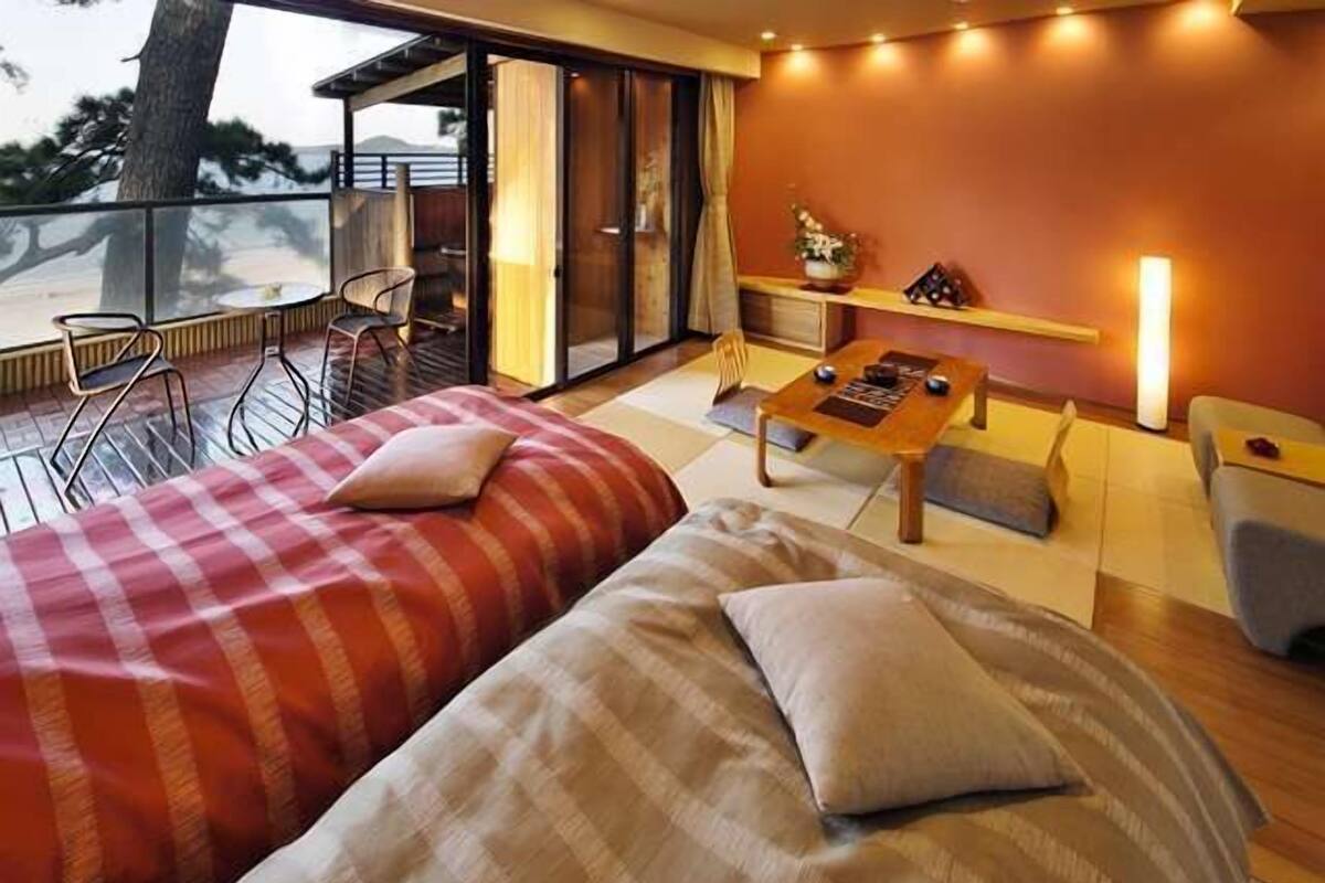 A modern bedroom with two beds, a small table, and a balcony with chairs.